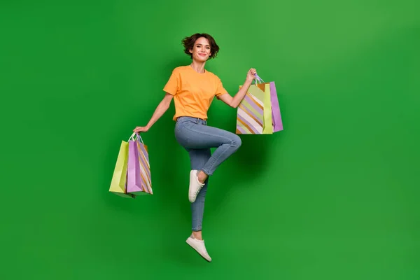 Full length photo of active overjoyed person jump arms hold packages isolated on green color background.