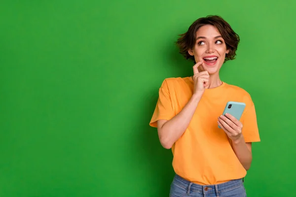 興奮した夢の若い女性の写真ドレスオレンジ色のTシャツチャット現代的なデバイス見て空のスペース隔離された緑の背景 — ストック写真