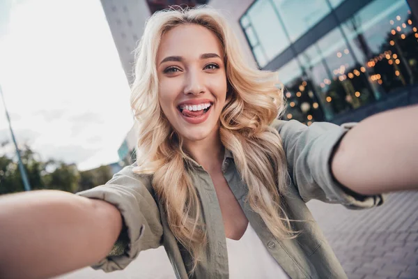 Self portrait of attractive cheerful funky wavy haired girl traveling showing tongue out fooling in town outdoors.