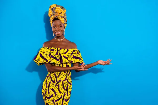 Photo of young sweet smiling african woman advertising product showing options isolated on blue color background.