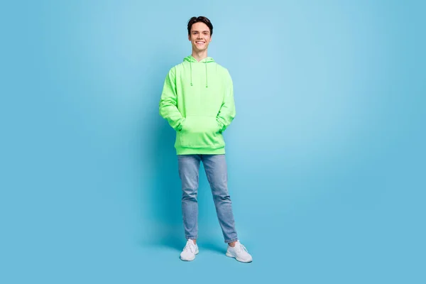 自信に満ちた魅力的な若い男の服を着た緑パーカーの腕ポケット笑顔隔離された青の色の背景 — ストック写真