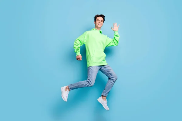 甘い魅力的な若い紳士の写真緑のスウェットシャツを着て笑顔ジャンプ高手孤立青の色の背景を振って — ストック写真