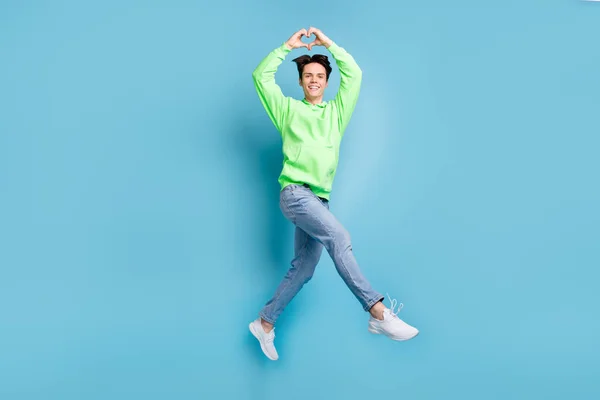 写真のロマンチックなボーイフレンドジャンプの指を見る心のシンボルは 緑のパーカージーンズの靴を着用隔離された青の色の背景 — ストック写真