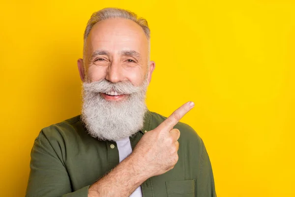 Photo portrait of elder man pointing blank space with finger recommending isolated vivid yellow color background.