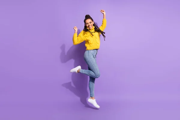 深褐色的女士跳着穿黄色毛衣牛仔裤运动鞋与紫色背景隔离的全长照片 — 图库照片
