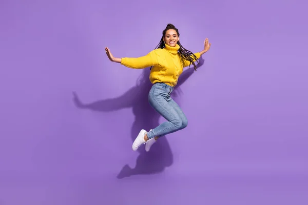 全长照片乐观的黑发女士跳舞穿着黄色毛衣牛仔裤运动鞋与紫色背景隔离 — 图库照片