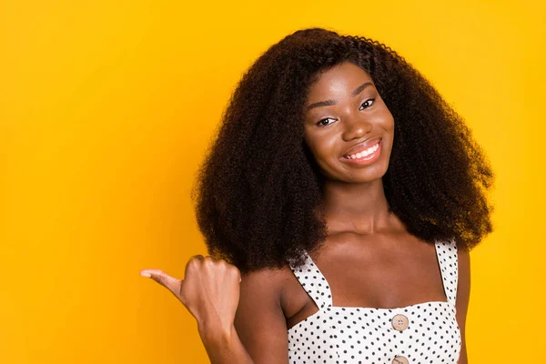 Photo of happy afro american lady point finger thumb empty space nice smile isolated on yellow color background.