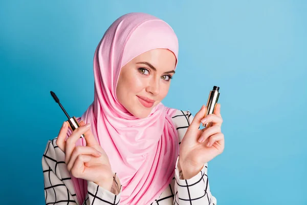 手の中に新しい装飾的なマスカラを保持しているかなり陽気な女性のムスリマの女の子のクローズアップ肖像画は 明るい青の色の背景に孤立 — ストック写真