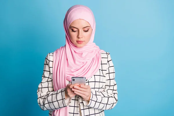 かなり深刻な焦点を当てたムスリマの女の子のポートレート使用デバイスガジェットチャット絶縁上の明るい青の色の背景 — ストック写真