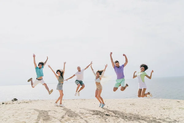 Full length photo of energetic carefree people have good mood jumping sand beach enjoy hang out outdoors.