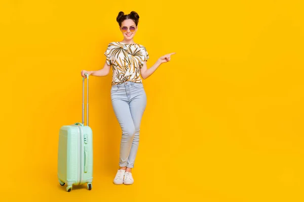 照片上穿着印花T恤的时髦女士拿着行李 指向空旷的空间 孤立的黄色背景 — 图库照片