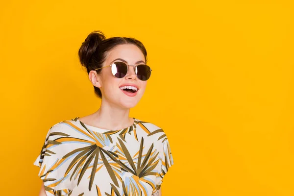 Photo of cute excited lady dressed print t-shirt dark glasses looking empty space isolated yellow color background.