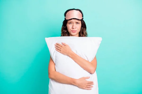 Photo of sleepy upset young lady nightwear hugging big white pillow isolated teal color background.
