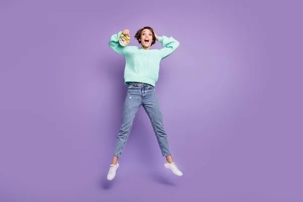 Full length body size photo of cheerful happy model jumping showing alarm clock amazed isolated pastel violet color background.