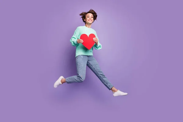 Full length body size photo of cheerful happy model jumping keeping red heart love symbol isolated pastel purple color background.