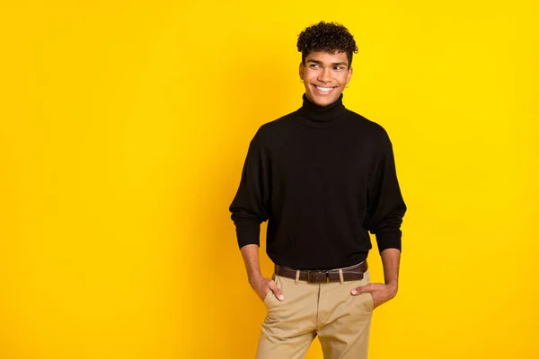Photo of confident cute dark skin guy dressed black turtleneck arms pockets looking empty space isolated yellow color background.