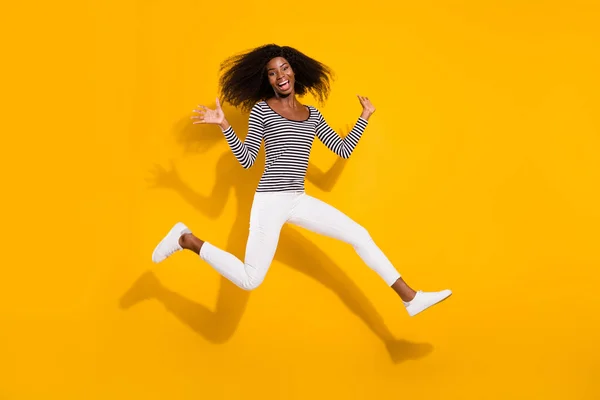 Full length body size photo woman in white pants jumping up laughing isolated vibrant yellow color background.