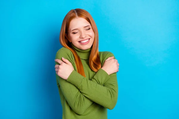 Photo of cheerful orange hair lady hug herself wear green sweater isolated on blue color background.