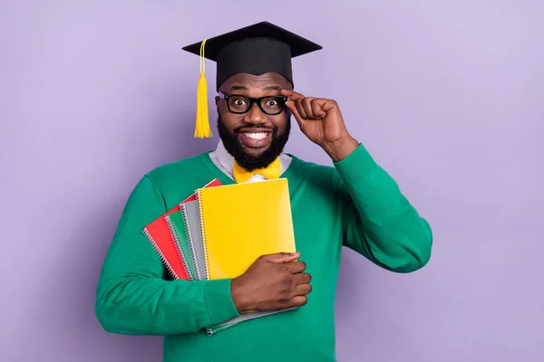 Portrait of positive handsome guy hold book notebook touch eyeglasses isolated on purple color background.