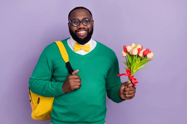 Photo of cheerful satisfied person carry backpack hold fresh flowers isolated on violet color background.