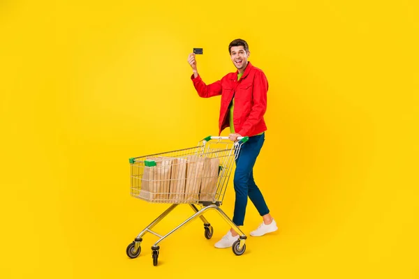 全长身材迷人的时髦快乐的男人手握卡片购物车 隔离在明亮的黄色背景下 — 图库照片