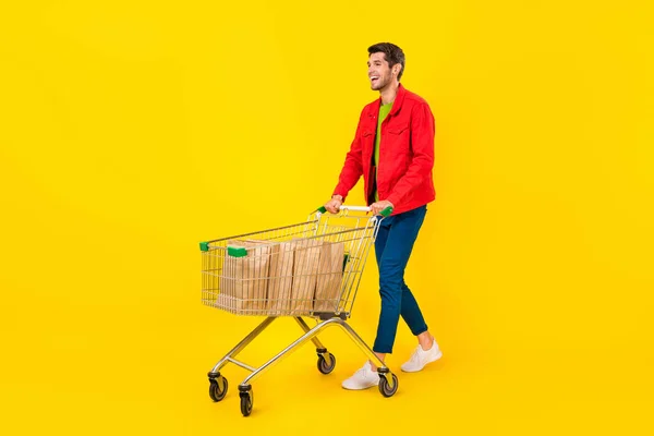 明るい黄色の背景に隔離された店のカート市場を運ぶ魅力的な陽気な男の完全な長さボディサイズビュー — ストック写真