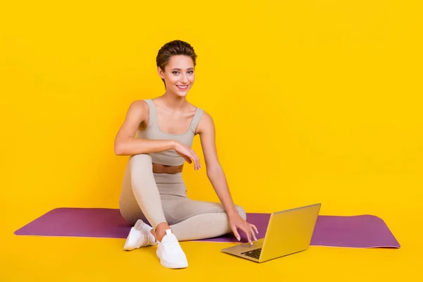 放松女士的照片坐垫使用上网本享受训练穿着灰色裁剪顶部孤立的黄色背景 — 图库照片
