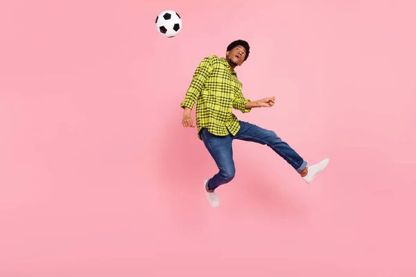 Full length photo of brunette man jump wear jeans look football isolated on pink color background.