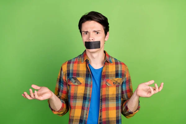 Portrait of attractive speechless clueless puzzled guy with sticker tape on mouth isolated over green color background.