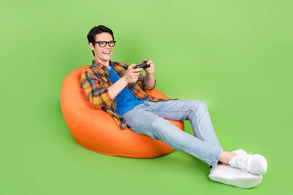 Photo of funny excited crazy guy hold gamepad play video game wear plaid shirt jeans shoes isolated green color background.