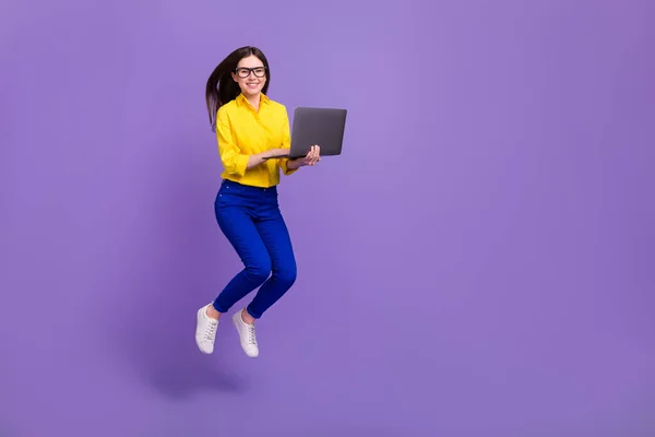 在明亮的紫色背景下 用笔记本电脑将漂亮的快乐女孩跳起来的全长体形图像分离出来 — 图库照片