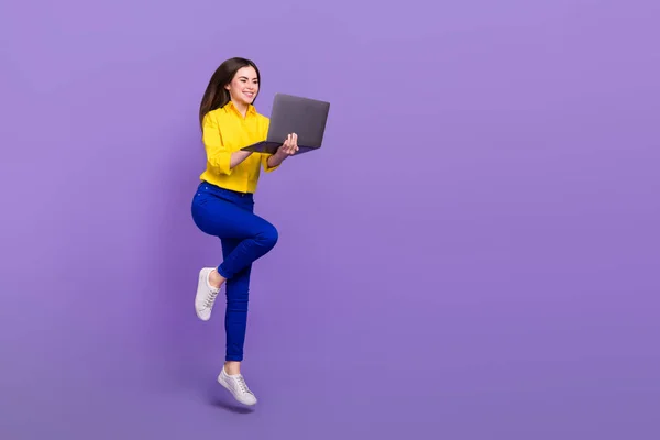 用笔记本电脑店购买与明亮紫罗兰色背景相隔离的全长身材美女跳跃图片 — 图库照片