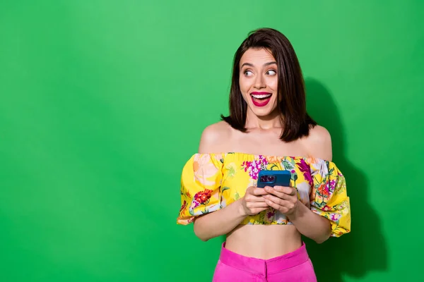 Photo of adorable excited lady wear off shoulders blouse looking empty space chatting modern gadget isolated green color background.