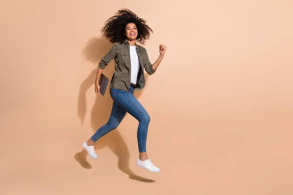 Full length body size view of attractive cheerful girl jumping carrying laptop running isolated over beige pastel color background.