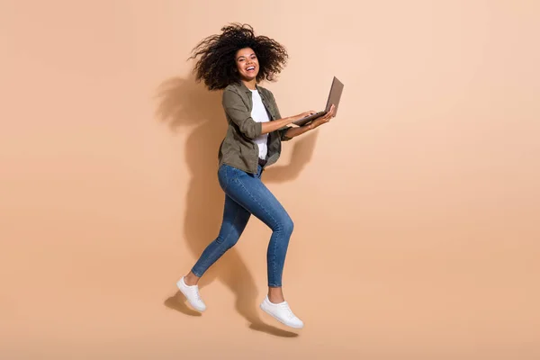 Full length body size view of attractive cheerful girl jumping using laptop having fun isolated over beige pastel color background.