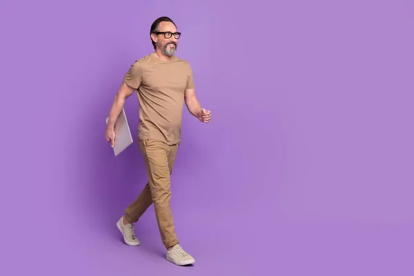 Full body profile side photo of aged man hold laptop go representative wear modern outfit isolated over violet color background.