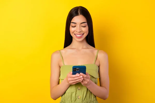 Photo of pretty cheerful girl hold use telephone typing write blog post isolated on yellow color background.