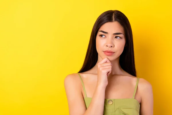 Photo of uncertain pretty young lady wear green outfit arm chin looking empty space isolated yellow color background.