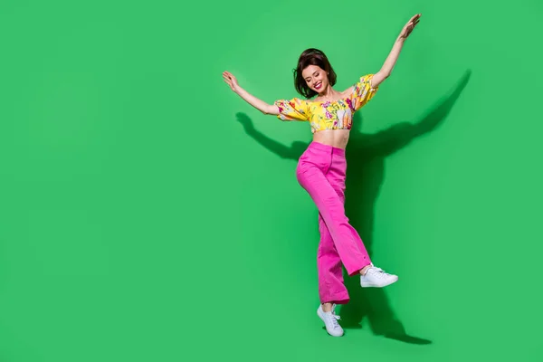 Full length photo of cute charming girl dressed off shoulders top jumping high walking empty space isolated green color background.
