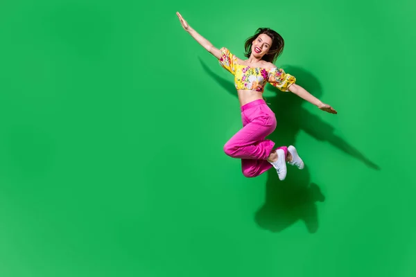 Full length photo of dreamy childish girl dressed off shoulders top jumping high arms sides empty space isolated green color background.