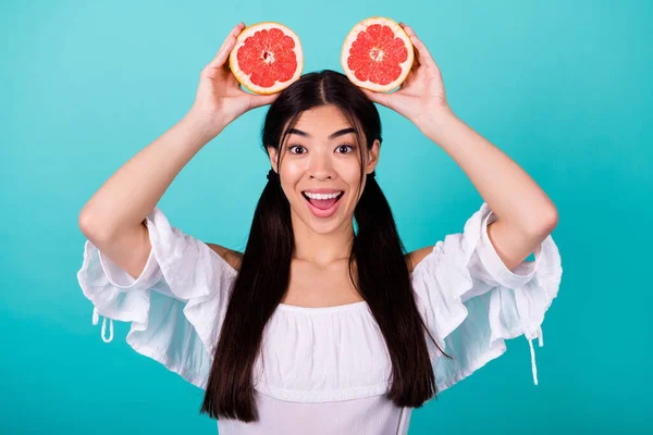 Photo of cute excited lady wear white holding two orange halves head smiling isolated turquoise color background.