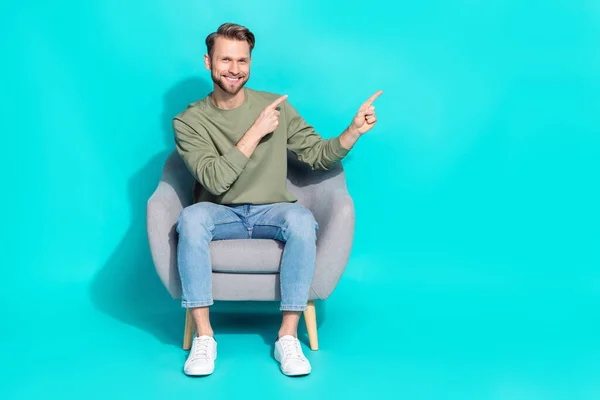Photo Cheerful Promoter Man Sit Armchair Direct Forefingers Empty Space — Stockfoto