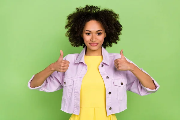 Portrait of good looking female showing thumbs-up rate good quality produce isolated on green color background.