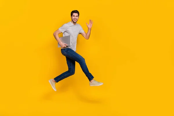 Full body profile photo of cool brunet millennial guy run with laptop wear t-shirt jeans footwear isolated on yellow background.