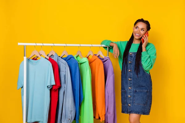 Photo of attractive cheerful girl speak communicate telephone store variety clothes isolated on yellow color background.