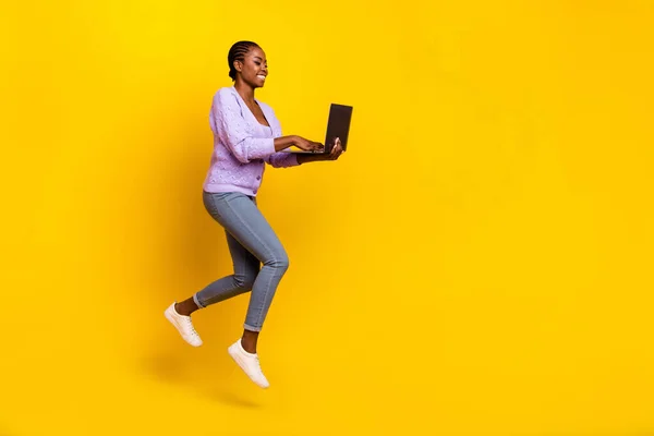 Full length profile photo of energetic person run jump use wireless netbook isolated on yellow color background.