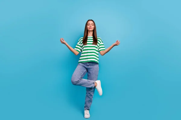 Full size photo of cute young lady do yoga wear green t-shirt jeans boots isolated on blue color background.