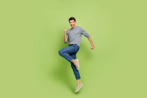 Full body photo of attractive carefree good mood man jumping in excitement triumph isolated on green color background.