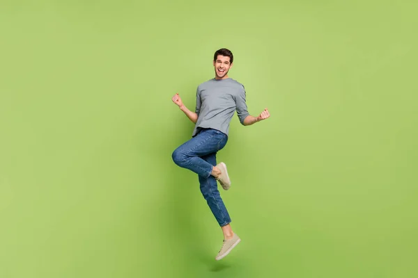 Full size photo of overjoyed ecstatic jumping positive man celebrate his victory isolated on green color background.