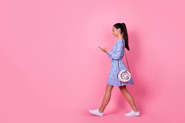 Full size profile photo of young attractive cute woman walking down street holding phone chatting isolated on pink color background.